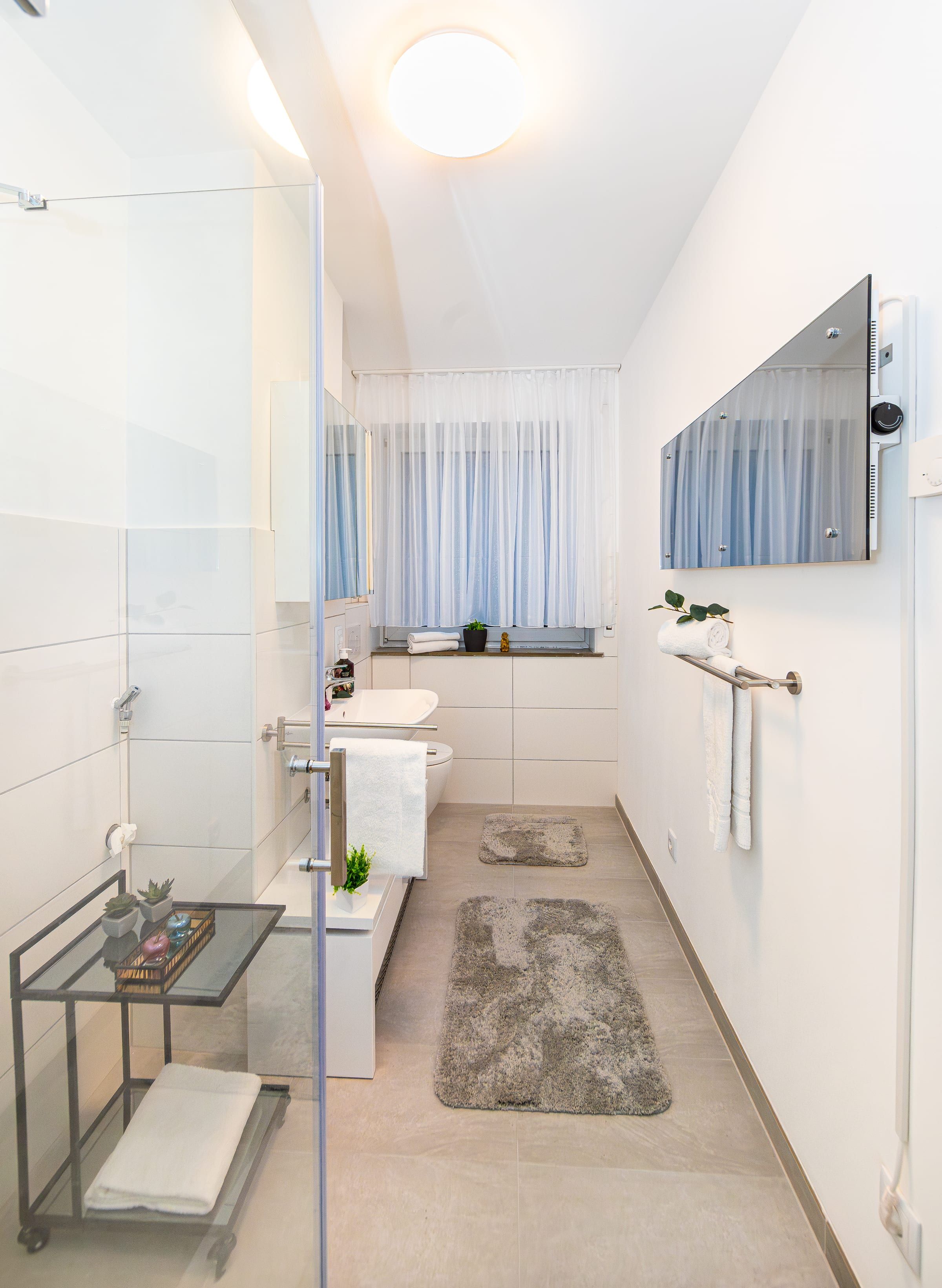 Längliches Bad mit Glasdusche auf der linken Seite und Fenster an der Stirnseite