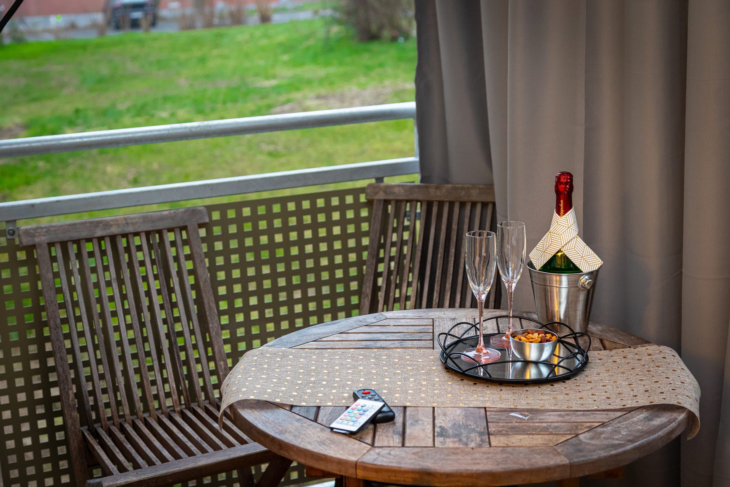 Balkon mit Holztisch und zwei Klappstühlen, Blick auf eine Rasenfläche