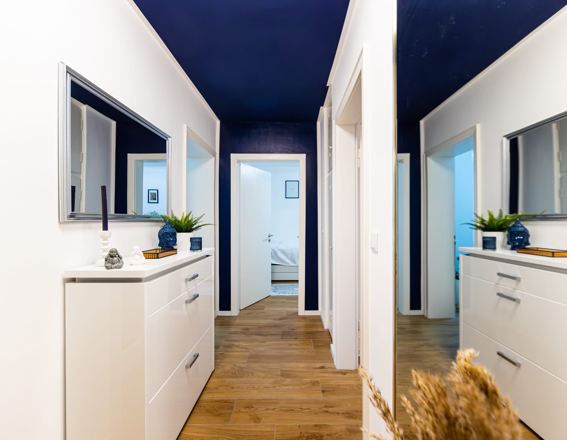 Flur mit dunkelblauer Decke, weißen Kommoden und Spiegeln, am Ende Blick in ein Schlafzimmer