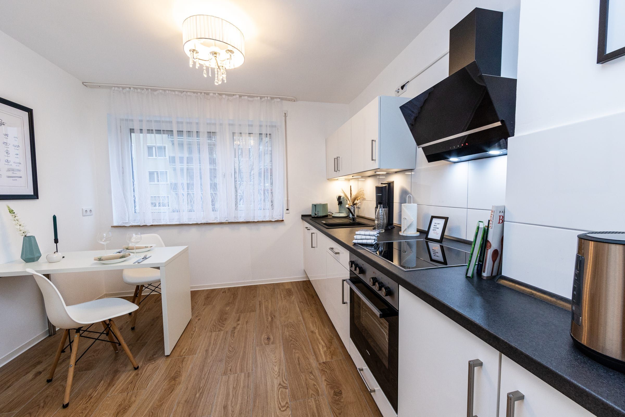 Küche mit weißen Schränken, dunkler Arbeitsplatte, Backofen und kleinem Esstisch am Fenster