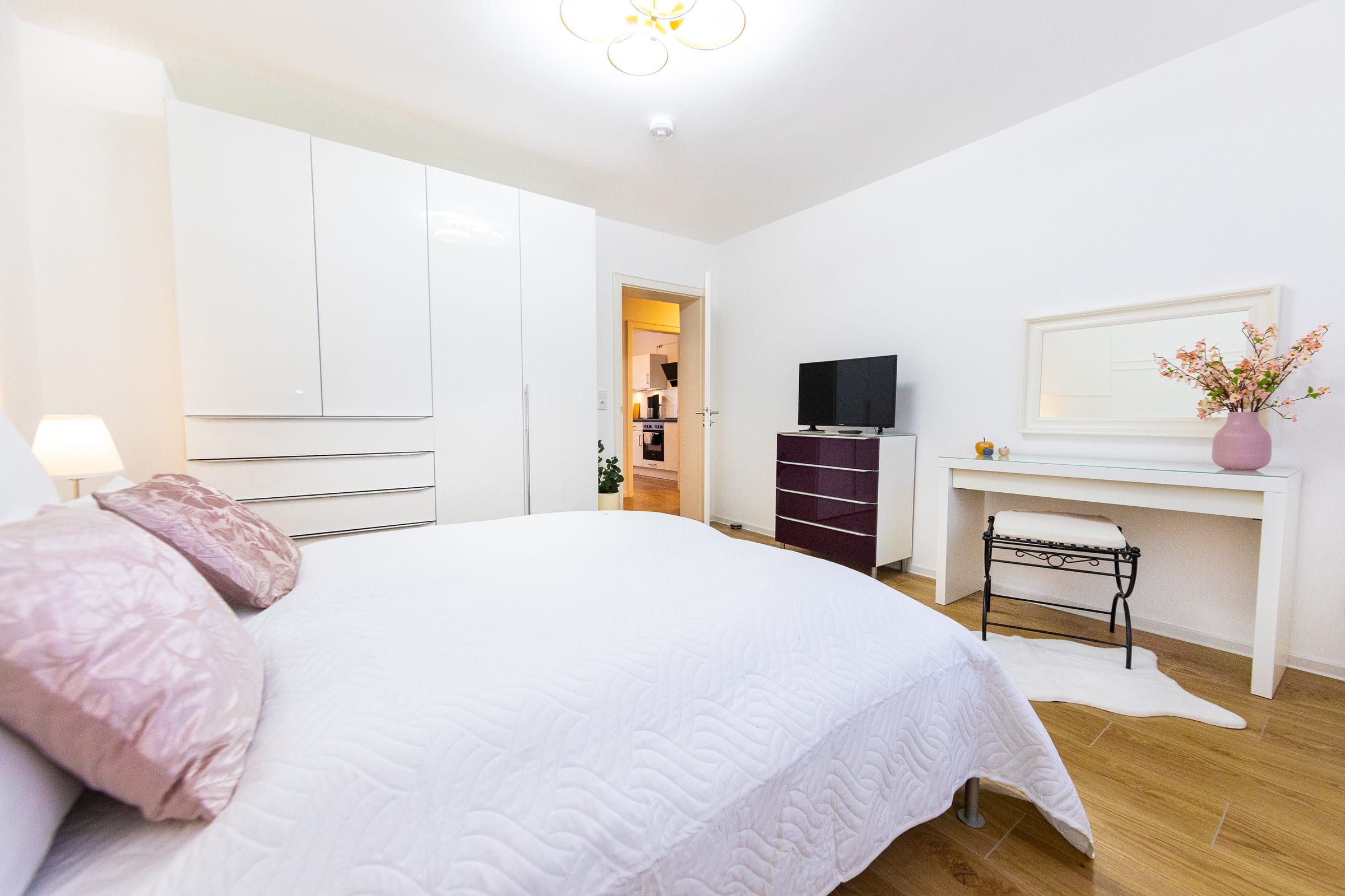 Schlafzimmer 1 mit Doppelbett, weißem Kleiderschrank, Kommode mit Fernseher und Schminktisch