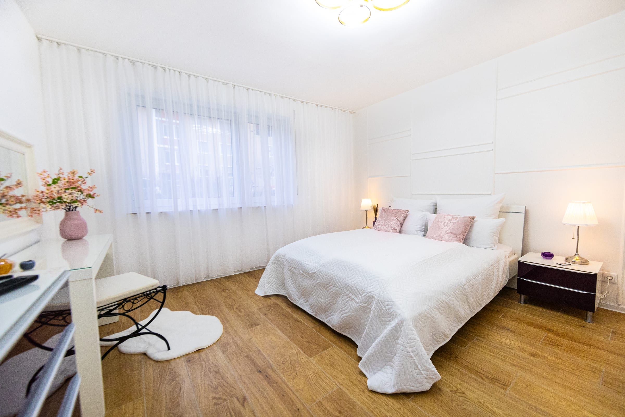 Schlafzimmer 1 mit Doppelbett, zwei Nachttischlampen und Schminktisch vor dem Fenster