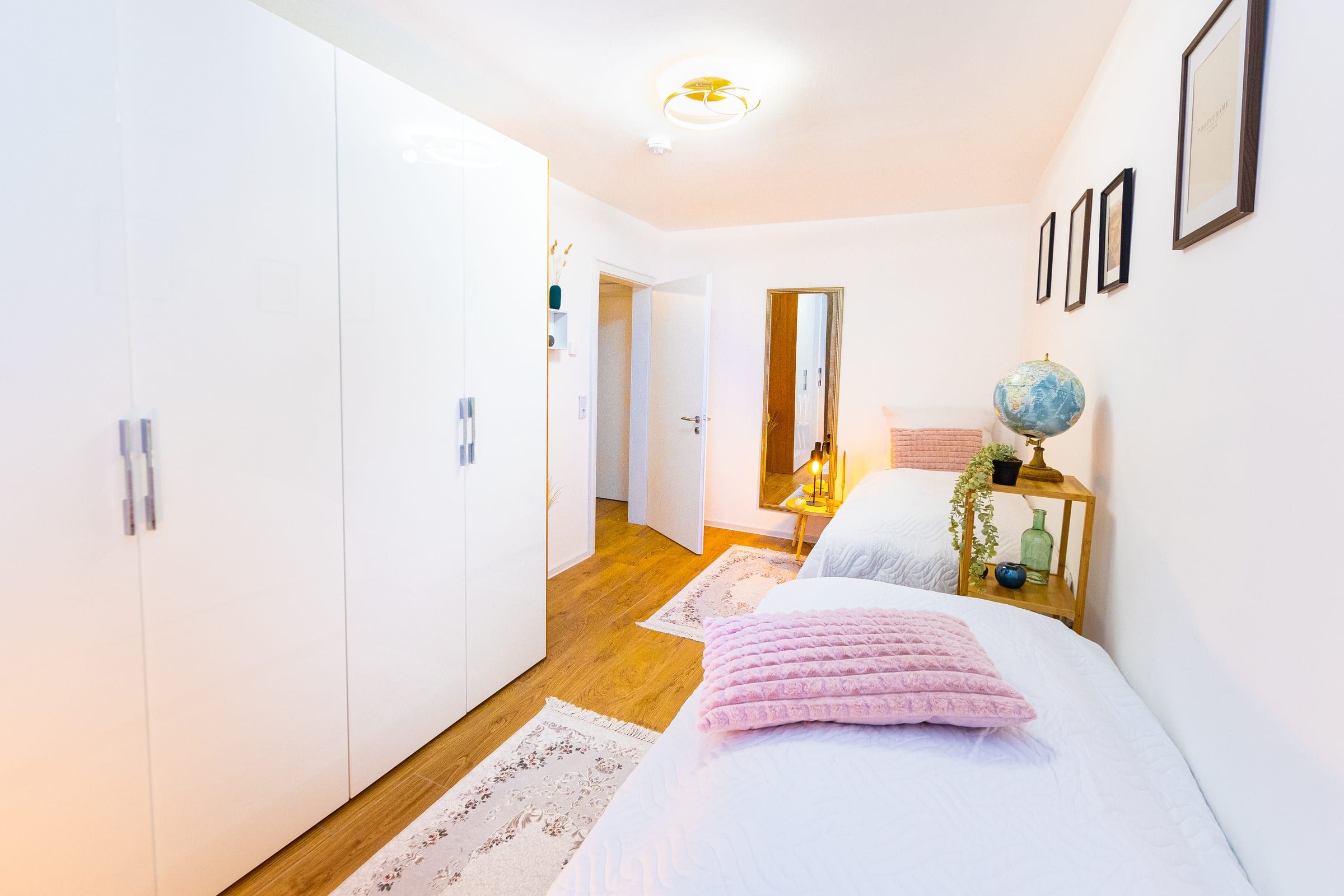 Schlafzimmer 2 mit großem weißem Kleiderschrank, zwei Einzelbetten und Holzregal mit Globus
