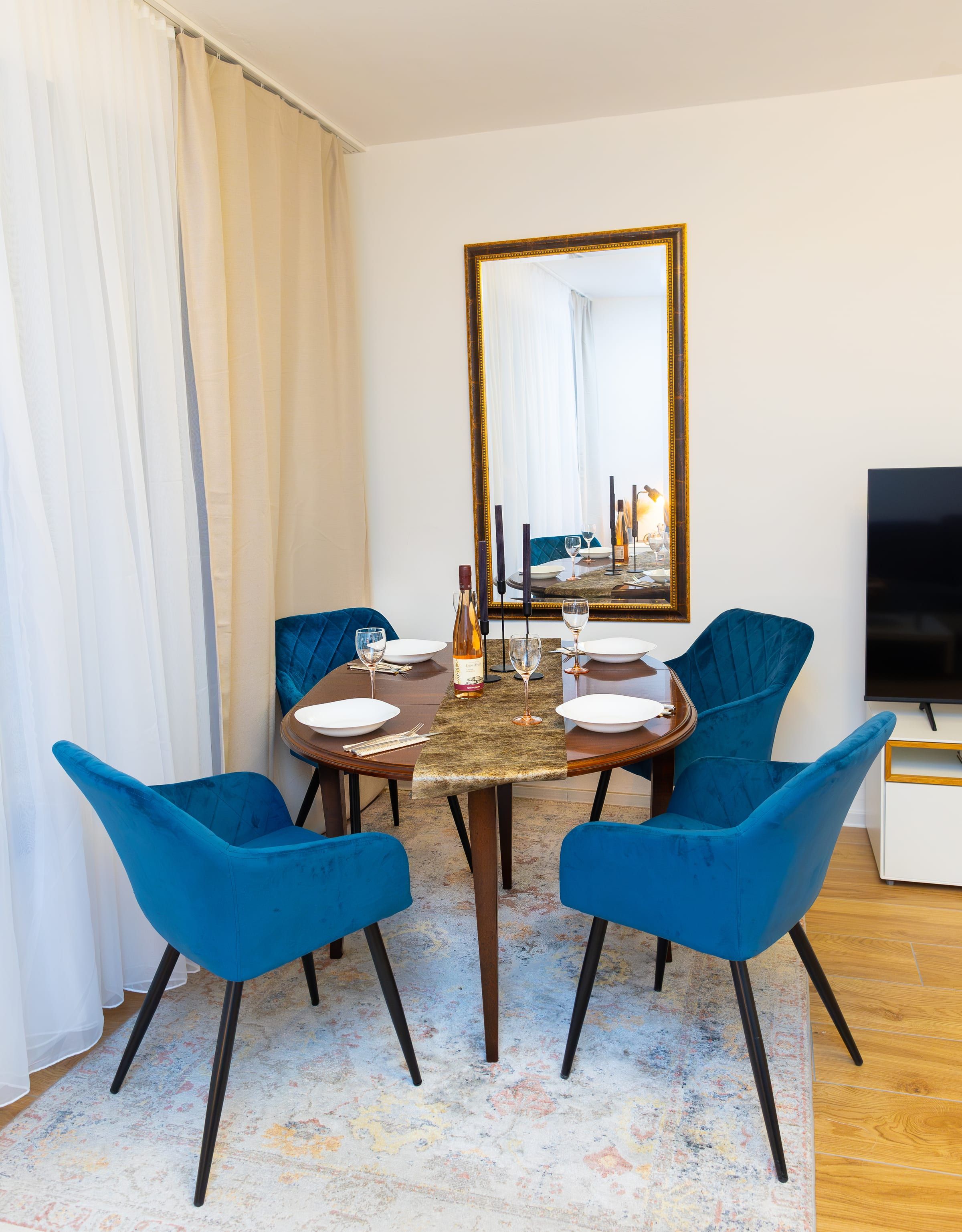 Esstisch mit vier blauen Samtstühlen vor einem großen Wandspiegel mit Goldrahmen