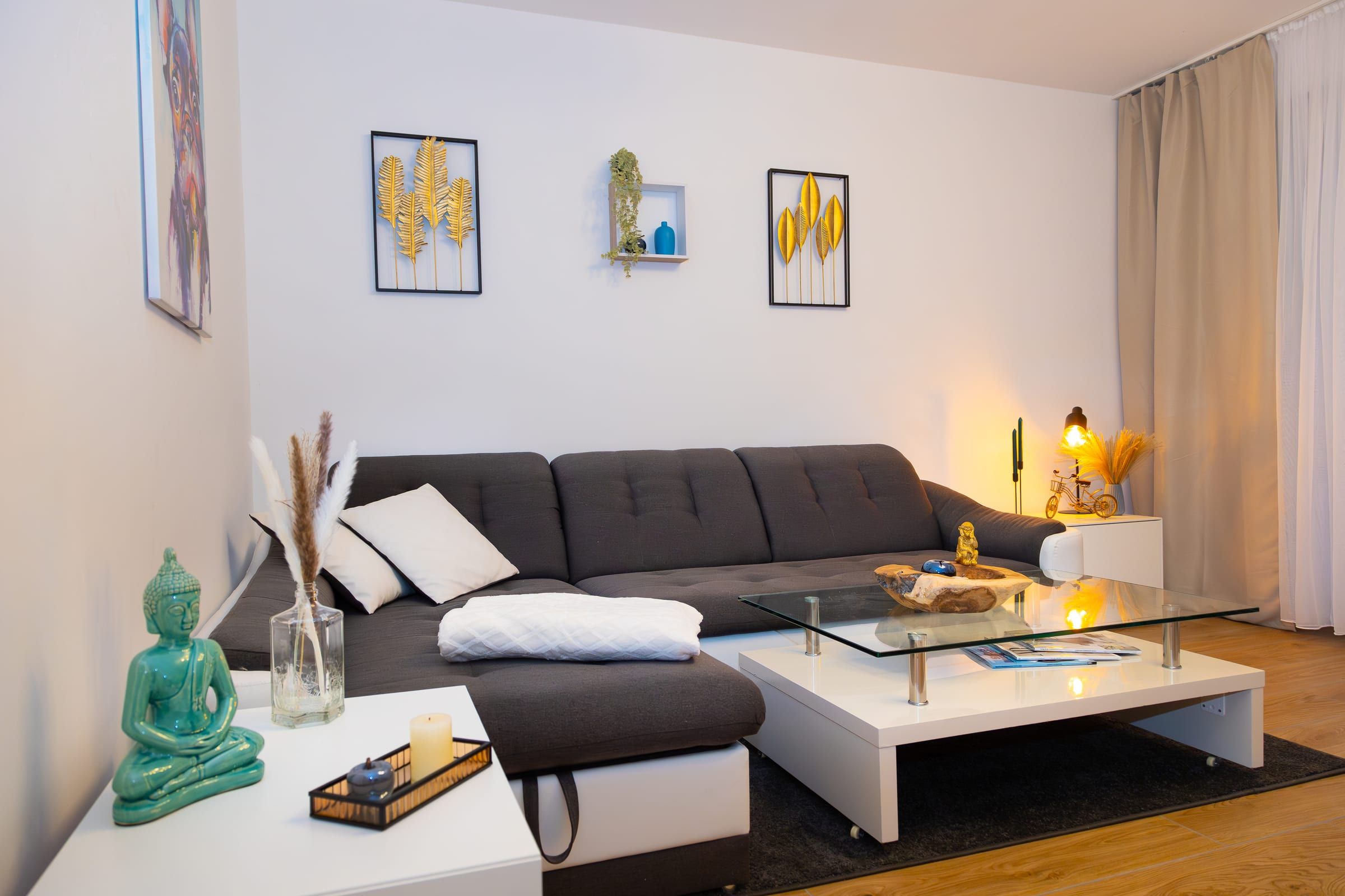 Sitzecke mit dunkelgrauem Ecksofa, Kissen und Decke, weißem Couchtisch und kleiner Tischlampe